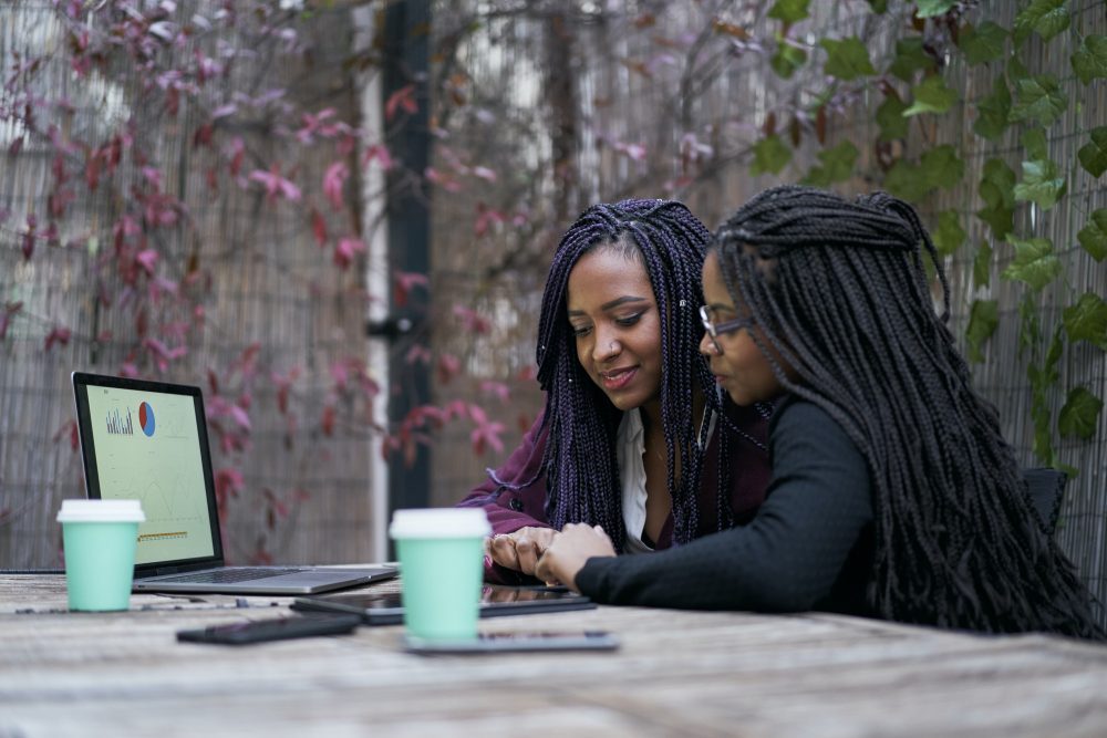Two African American women sitting on a terrace outside working on the laptop. Concept of teamwork.